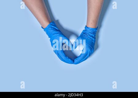 Mains du médecin dans des gants médicaux bleus en forme de coeur sur fond bleu avec espace de copie. Banque D'Images