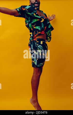 Homme afro-américain moyen adulte barbu souriant et dansant portant un short et une chemise hawaïens sur une photo studio de saut de vacances Banque D'Images