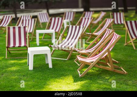 Chaises longues à rayures et table dans le parc sur l'herbe. Le concept de loisirs et d'activités de plein air. Banque D'Images