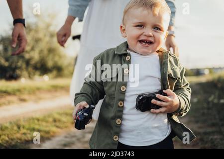 Un garçon tout-en-un drôle tenant des jouets entre les mains et courant loin de ses parents à l'extérieur Banque D'Images