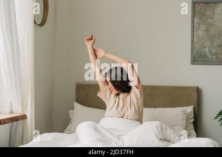 Jeune femme latine reposée se réveillant joyeusement matin dans une chambre lumineuse minimaliste Banque D'Images