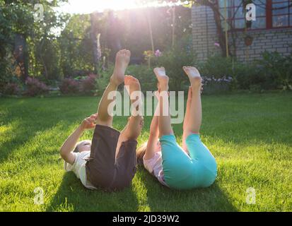 Deux enfants pieds nus s'étendent sur l'herbe avec leurs pieds vers le haut. Promenade gaie dans le parc lors d'une journée ensoleillée d'été. Ambiance d'été, bonne enfance. Rétroéclairage ab Banque D'Images