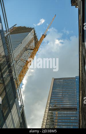 Un gratte-ciel en construction dans un quartier d'affaires d'un centre-ville par une journée ensoleillée et quelques nuages entourés de bâtiments plus anciens. Banque D'Images