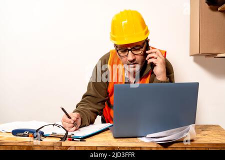 L'entrepreneur parle au téléphone cellulaire tout en vérifiant l'ordinateur portable et en prenant des notes sur ce qu'il parle au bureau de travail. Concept d'organisation du travail, télétravail Banque D'Images