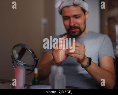 Concept de beauté pour hommes. Un homme de race blanche qui vérifie sa peau. Un homme à la barbe tire la crème de soin de la peau, les mains des hommes utilisant la crème hydratante, la peau et les soins des mains. Banque D'Images