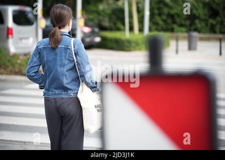 Une femme avec un sac de shopping est vue attendre de traverser la rue Swietokrzyska avec un panneau de sécurité en construction roadworks au premier plan à Varsovie Banque D'Images