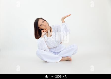 Belle femme relaxante aux cheveux bruns penchée à la main dans lotus poser en studio blanc. Promotion du produit. Copier l'espace Banque D'Images