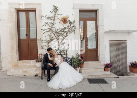 Portrait de mariage, couple marié amoureux, assis sur le banc près des portes de l'église. Plantes et arbre sur le mur Banque D'Images
