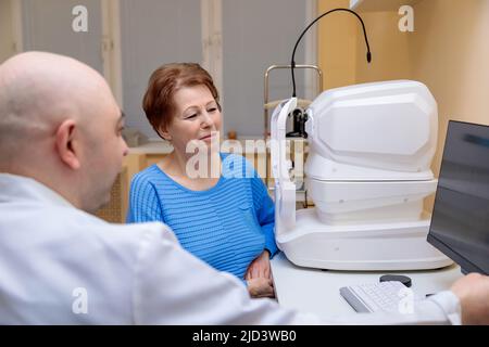 Un ophtalmologiste masculin explique les résultats d'un examen oculaire à une femme adulte, montrant un dessin sur un ordinateur. Banque D'Images