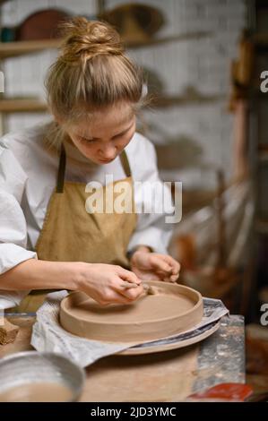 Un céramiste fait une plaque d'argile Une femme dans un tablier travaille dans un atelier de poterie. Banque D'Images