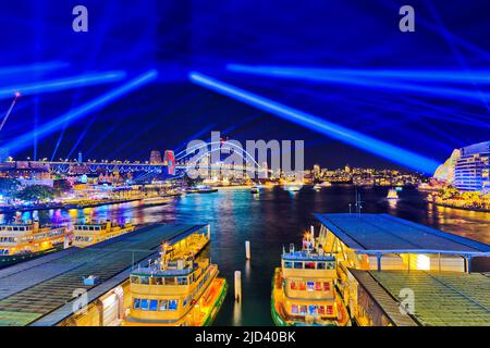 Les passagers du ferry circulaire sur quai se déferent lors du spectacle lumineux de Vivid Sydney sous un ciel lumineux éclairé par un spectacle laser. Banque D'Images