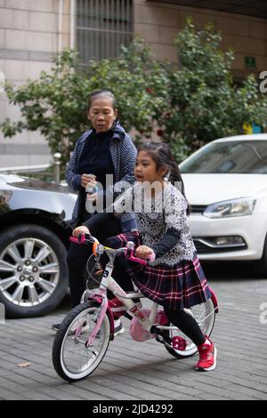 Une fille indonésienne et sa grand-mère vêtues d'un thème de printemps, un vélo BTWIN rose au printemps, dans la rue d'un complexe d'appartements à Shanghai Banque D'Images