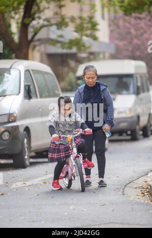 Une fille indonésienne et sa grand-mère vêtues d'un thème de printemps, un vélo BTWIN rose au printemps, dans la rue d'un complexe d'appartements à Shanghai Banque D'Images