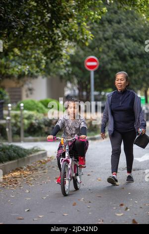 Une fille indonésienne et sa grand-mère vêtues d'un thème de printemps, un vélo BTWIN rose au printemps, dans la rue d'un complexe d'appartements à Shanghai Banque D'Images