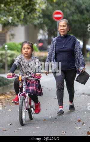 Une fille indonésienne et sa grand-mère vêtues d'un thème de printemps, un vélo BTWIN rose au printemps, dans la rue d'un complexe d'appartements à Shanghai Banque D'Images