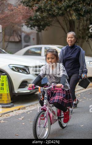 Une fille indonésienne et sa grand-mère vêtues d'un thème de printemps, un vélo BTWIN rose au printemps, dans la rue d'un complexe d'appartements à Shanghai Banque D'Images