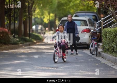 Une fille indonésienne et sa grand-mère vêtues d'un thème de printemps, un vélo BTWIN rose au printemps, dans la rue d'un complexe d'appartements à Shanghai Banque D'Images