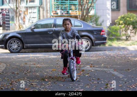 Une fille indonésienne et sa grand-mère vêtues d'un thème de printemps, un vélo BTWIN rose au printemps, dans la rue d'un complexe d'appartements à Shanghai Banque D'Images