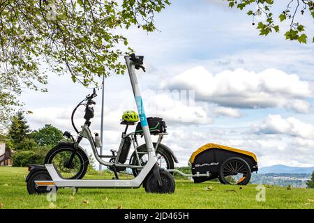 Everett, WA - Etats-Unis -06-04-2022: Scooter électrique en vélo de terrain et utilitaire avec Burley Cargo Trailer en arrière-plan, deux alternative transpo Banque D'Images