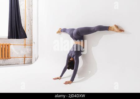 Femme pratiquant le yoga, exécute l'exercice Adho Mukha Vrikshasana avec Samakonasana, se tient sur ses mains avec une ficelle transversale, penchée son corps a Banque D'Images