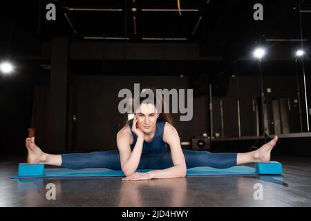 Une jeune femme mince fait un peu de ficelle pour étirer ses jambes. Une femme joyeuse qui fait les fractionnements. Une fille de fitness s'étirant sur un tapis de yoga. Femme sportive Banque D'Images