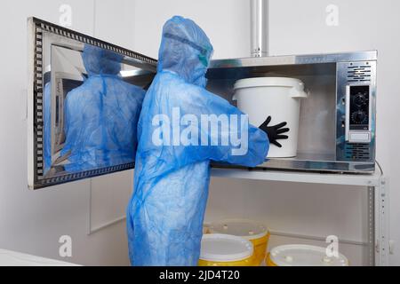 Technologue portant un vêtement de protection EPI, un masque, des gants et travaillant avec un grand seau en plastique dans un laboratoire de recherche Banque D'Images