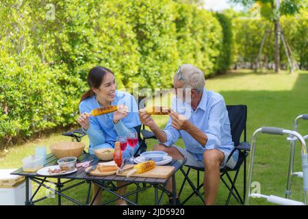 Caucasiens handicapés personnes âgées avec mobilité marcheur campant avec femme asiatique aidants dans le jardin à la maison pour se détendre et l'expérience de la nature dans la somme Banque D'Images