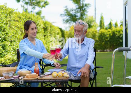 Caucasiens handicapés personnes âgées avec mobilité marcheur campant avec femme asiatique aidants dans le jardin à la maison pour se détendre et l'expérience de la nature dans la somme Banque D'Images