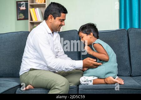 Le père câlin sa petite fille après être venu du bureau à la maison tout en étant assis sur un canapé - concept de temps en famille, détente et parent ludique Banque D'Images