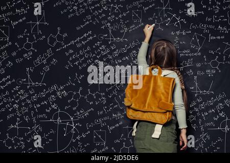 Fille d'enfant contre grand tableau noir avec des formules, vue arrière Banque D'Images