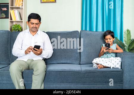 Père et fille sur le canapé occupé séparément à utiliser le téléphone mobile à la maison - concept de la fracture numérique, les médias sociaux et la dépendance technologique Banque D'Images
