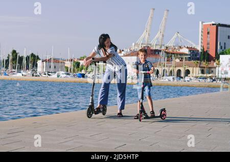 Mode de vie familial et concept de vacances heureux. Mère, petit garçon, fille, scooter d'équitation, marche dans la vieille ville, rue. Rire un jour ensoleillé d'été. Banque D'Images