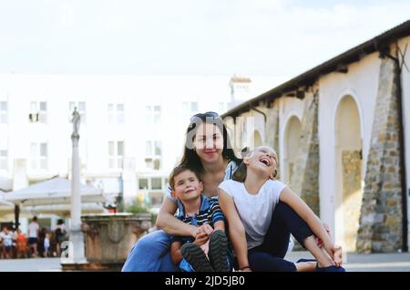 Mode de vie familial et concept de vacances heureux. Mère, petit garçon, fille assise, marche dans la vieille ville, rue. Rire un jour ensoleillé d'été. Amuse-toi bien Banque D'Images