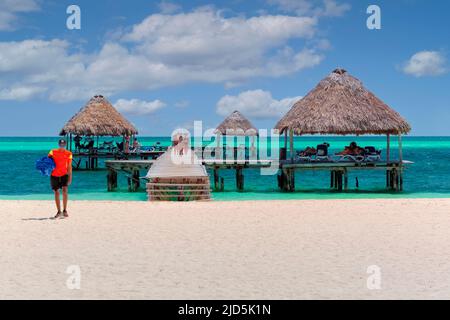 Un jeune homme marchant sur une belle plage avec des gens debout sur une jetée en bois à Cayo Guillermo, Cuba Banque D'Images