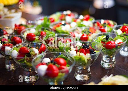 Petites portions de cocktail de salade de tomates cerises, boules de mozzarella, laitue Lolo Rosso. Beaucoup de portions dans une portion de verre. Disposition de la restauration. Banque D'Images