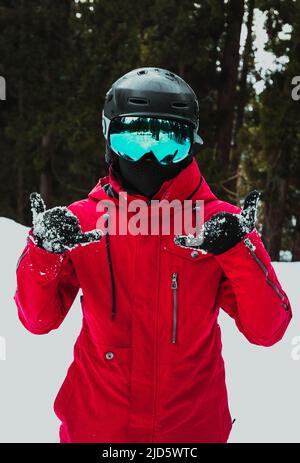 homme sur une montagne enneigée en veste rouge, casque noir et lunettes de ski bleues Banque D'Images