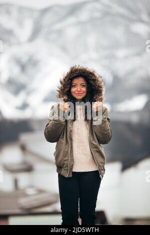 jeune femme hispanique en parka à fourrure verte en hiver froid avec fond de montagne flou Banque D'Images