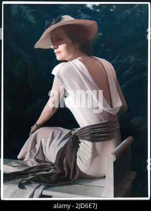 Une femme est assise sur un banc au soleil, portant une robe de manteau blanche avec un dos bas et une ceinture de velours; elle a une veste et un chapeau assortis version colorisée de : 10082896 Date: 1930s Banque D'Images