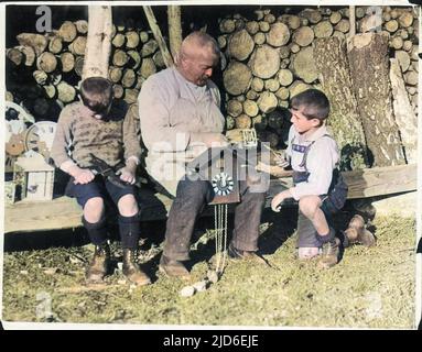 Deux petits garçons aident un vieux horloger, peut-être leur grand-père, à faire un cuckoo horloge dans la Forêt Noire, en Allemagne. Version colorisée de : 10155071 Date: 1930s Banque D'Images