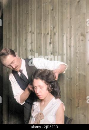 Un coiffeur de sexe masculin coupe les cheveux d'une jeune femme. Version colorisée de : 10164560 Date : début 1930s Banque D'Images