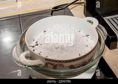 Le sucre en poudre, le beurre de cacao et le cacao râpé dans un récipient pour faire du chocolat sont chauffés dans un bain d'eau. Banque D'Images