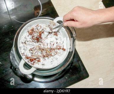 Le sucre en poudre, le beurre de cacao et le cacao râpé dans un récipient pour faire du chocolat sont chauffés dans un bain d'eau. Banque D'Images