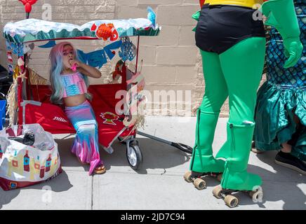 Coney Island, États-Unis. 18th juin 2022. Une jeune fille habillée comme une sirène a un snack à l'ombre tout en attendant que son roller skate portant le père pour la tirer dans le défilé. Le Coney Island Mermaid Parade est le plus grand défilé d'art des États-Unis. La parade célèbre le début de l'été. Les fêtards s'habillent comme des méraides, des poissons et d'autres créatures marines. (Photo par Aimee Dilger/SOPA Images/Sipa USA) crédit: SIPA USA/Alay Live News Banque D'Images