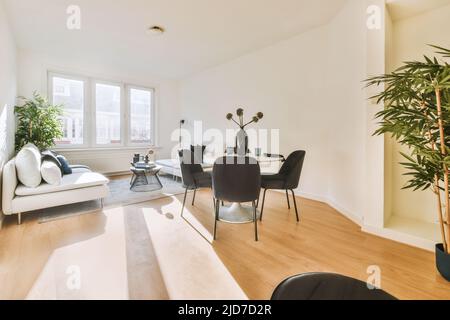 Décoration intérieure élégante d'un salon spacieux avec de grandes fenêtres et des murs blancs avec des canapés confortables et une table sur une moquette sur un sol en parquet et des salles à manger dans une maison moderne Banque D'Images