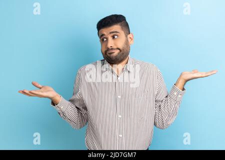 Je ne sais pas. Portrait d'un homme d'affaires perplexe et perplexe, incertain, n'a pas de réponse, portant une chemise rayée. Studio d'intérieur isolé sur fond bleu. Banque D'Images