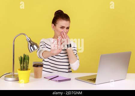 Une employée de bureau mécontente qui se tenait à respirer, se pinçant le nez avec les doigts, confondue avec une odeur dégoûtée, ne veut pas respirer. Studio d'intérieur tourné isolé sur fond jaune. Banque D'Images