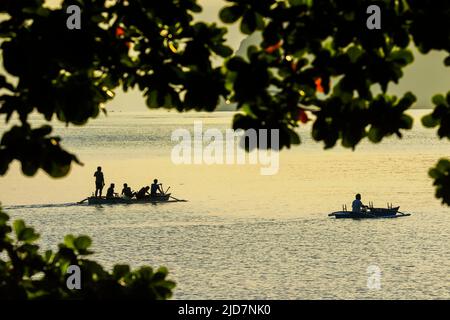 Coucher de soleil à l'est avec des pêcheurs en canoës et sur l'île de Buhias depuis la plage de Kalea sur Siau. Kalea, île de Siau, archipel de Sangihe, Sulawesi du Nord, Indonésie Banque D'Images