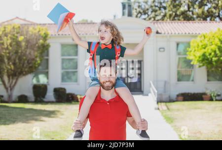 L'homme et l'enfant heureux stupéfié de pigeyback près de l'école. Père marchant fils à l'école. Parent et élève de l'école primaire garçon avec sac à dos. Banque D'Images