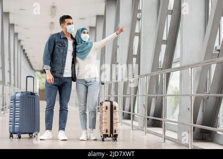 Jeunes conjoints musulmans en masques médicaux debout avec des bagages à l'aéroport Banque D'Images