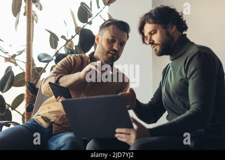 Des collègues masculins focalisés travaillant ensemble sur un projet professionnel, utilisant des ordinateurs portables et des tablettes dans un bureau moderne Banque D'Images